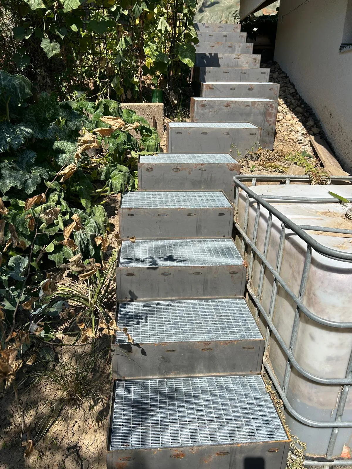Reihe einzelner Stufenmodule mit Gitterrost entlang eines Gartenbeets.